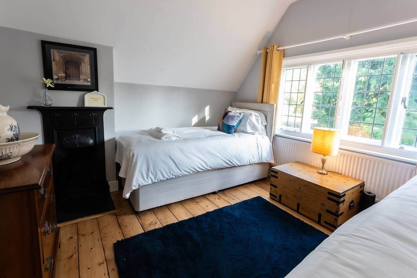 A bedroom with a bed, bedside table, lamp, dresser, and window with curtains.