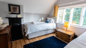 A bedroom with a bed, bedside table, lamp, dresser, and window with curtains.