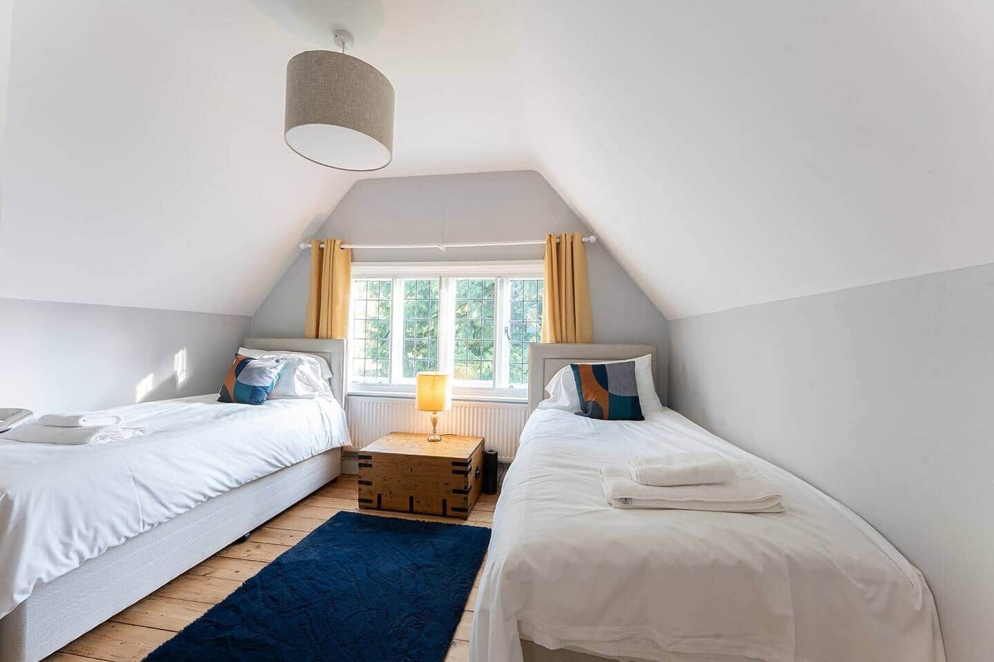 Ein Schlafzimmer mit zwei Einzelbetten, einem Holz-Nachttisch, einer Lampe und einem Fenster mit Vorhängen.