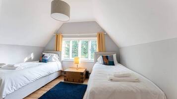 Ein Schlafzimmer mit zwei Einzelbetten, einem Holz-Nachttisch, einer Lampe und einem Fenster mit Vorhängen.