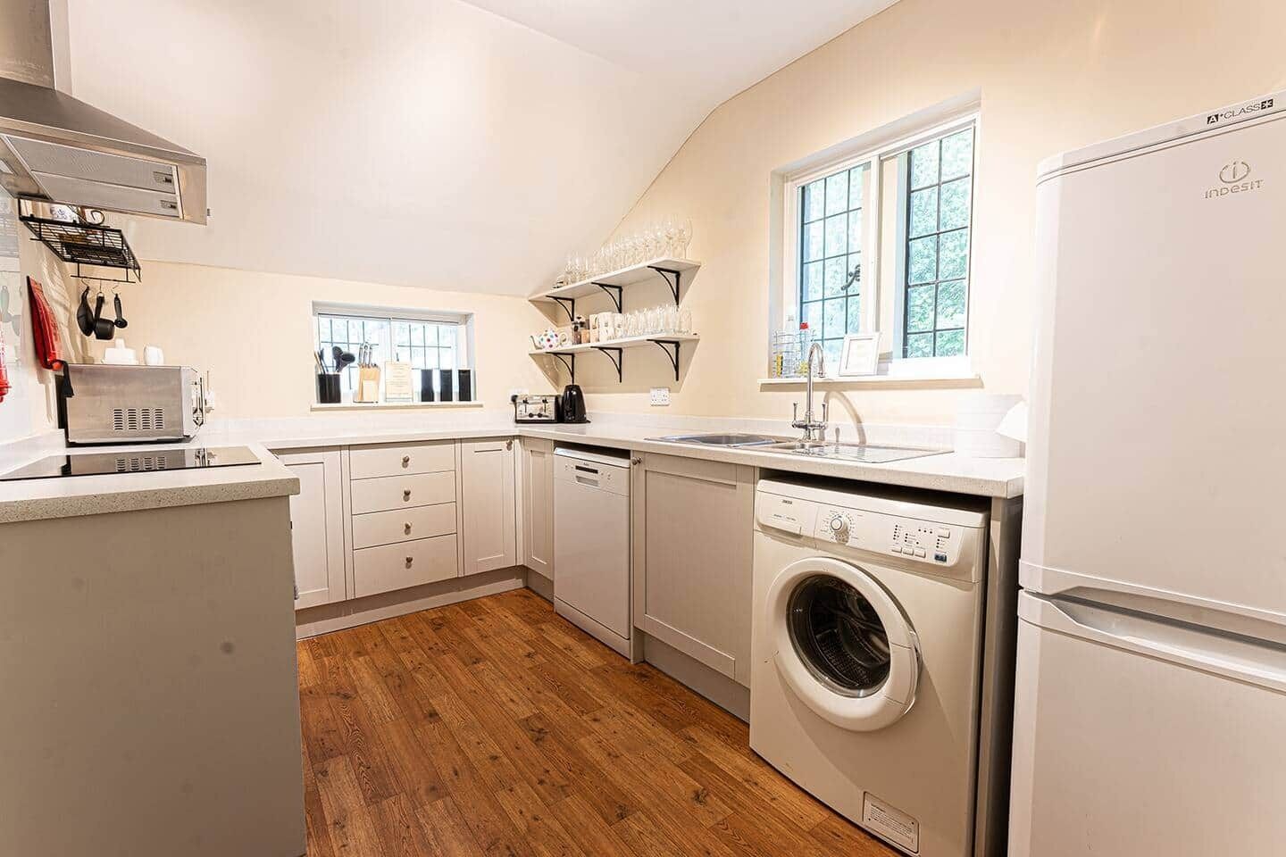 A compact kitchen with white cabinets, a built-in dishwasher, a washing machine, and a refrigerator.