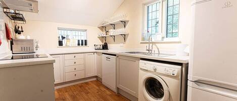 A compact kitchen with white cabinets, a built-in dishwasher, a washing machine, and a refrigerator.