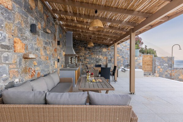 Eine Terrasse im Freien mit Steinmauern, Korbmöbeln und Grillplatz.