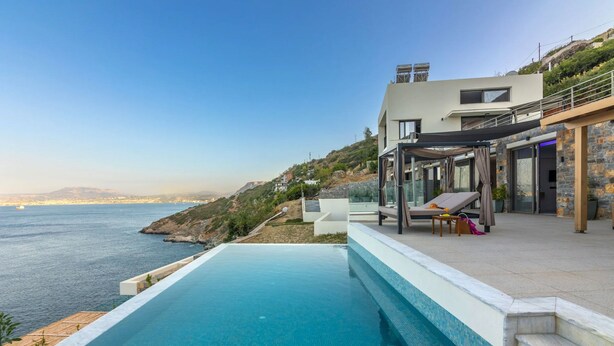 A modern poolside area with a clear view of the sea, a covered seating area, and a stone facade. - Euphoria Villa Crete (Malevizi)