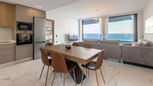 A modern kitchen with a dining area, a sofa, and a large window with a view. - Euphoria Villa Crete (Malevizi)