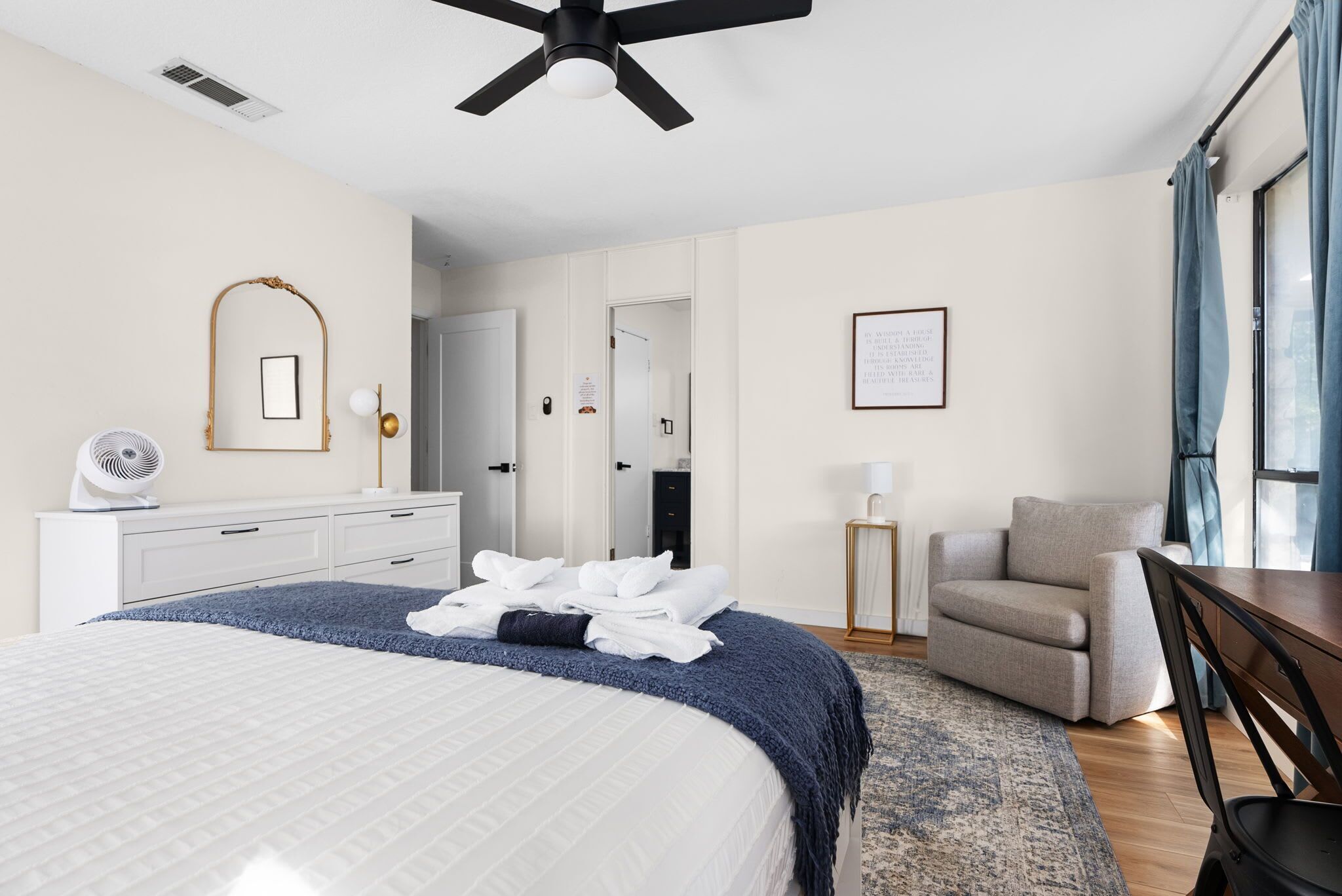 A modern hotel room with a large bed, a ceiling fan, a desk, and a chair.