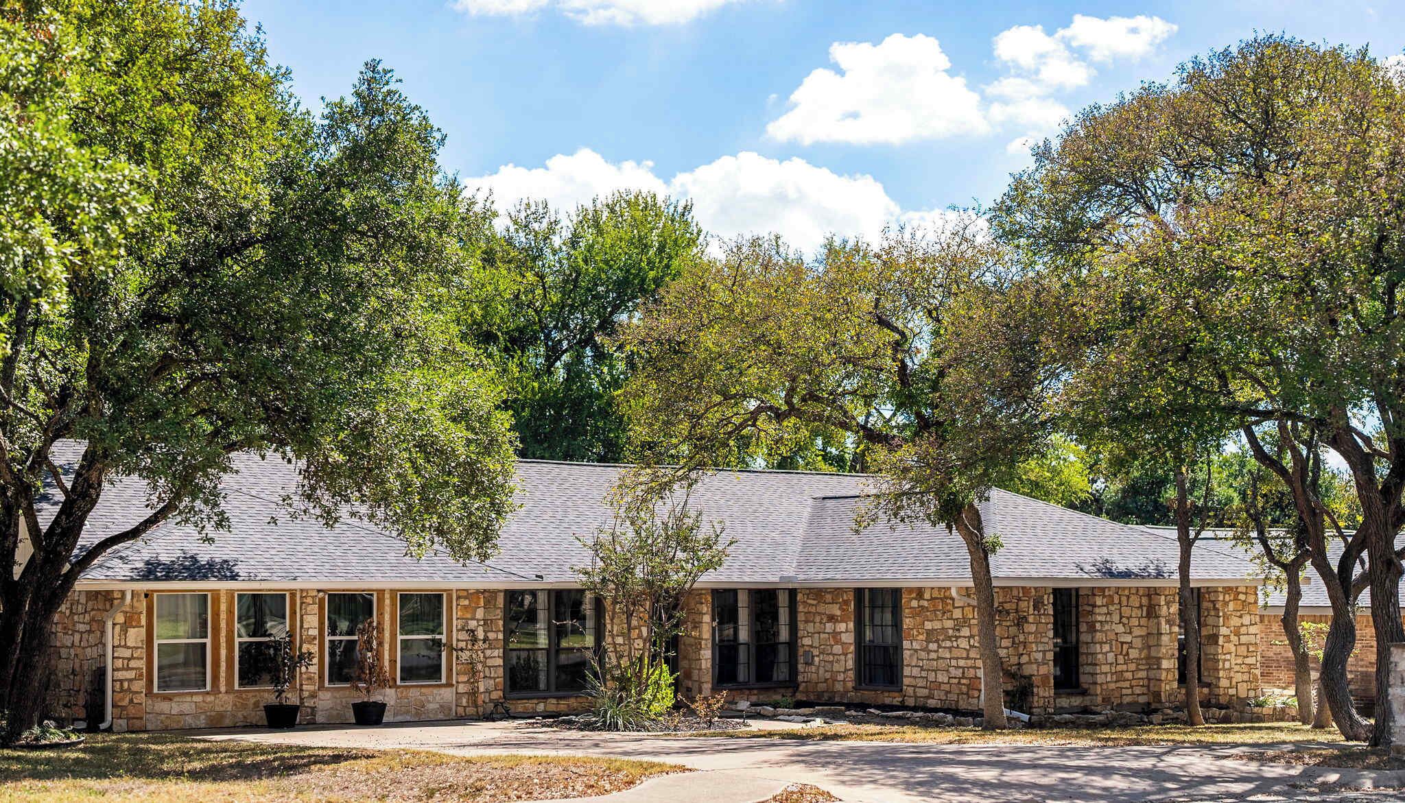 A stone building with multiple windows, surrounded by trees.