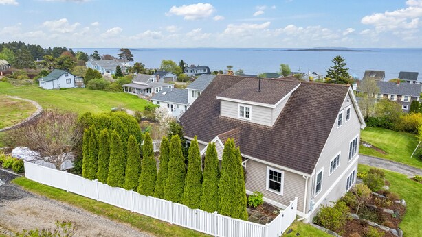A two-story house with a dark roof, surrounded by a white fence and tall evergreen trees.