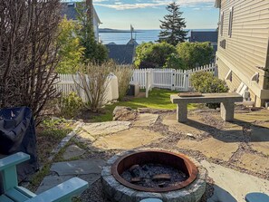 A backyard with a fire pit, a white picket fence, and a view of the water. - Oceanside Oasis, New Listing, Steps from the Ocean, Perfect Bailey Isl Escape (Bailey Island)