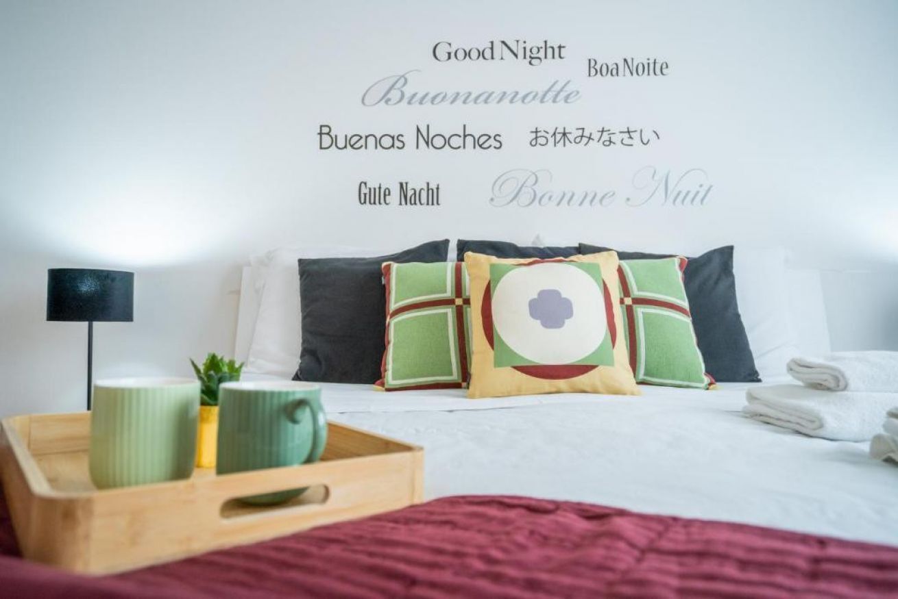 Een net opgemaakt bed met kussens, een nachtkastje met een lamp en een schaal groene mokken.