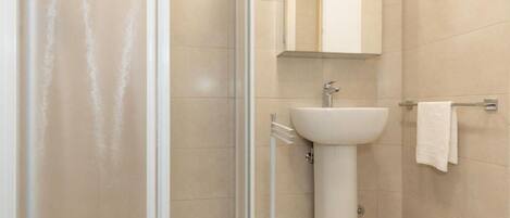 A bathroom with a glass shower enclosure, a pedestal sink, and a towel rack.