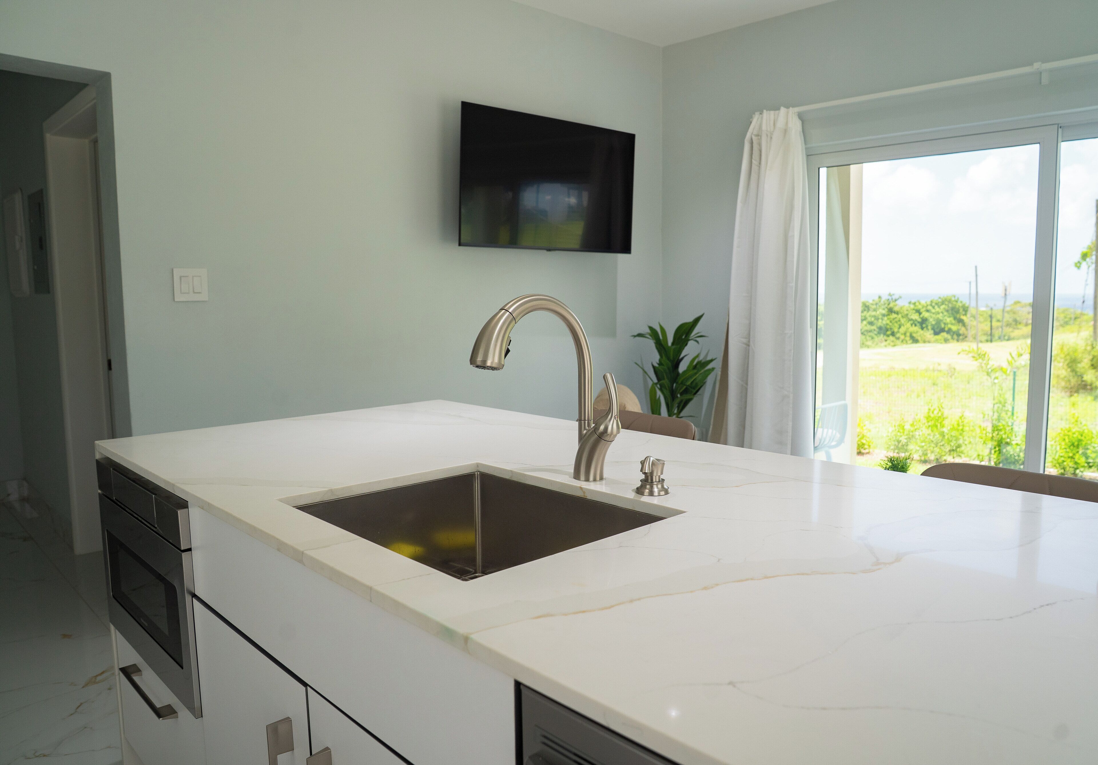 A modern kitchen with a large island, stainless steel appliances, and a view of greenery outside.