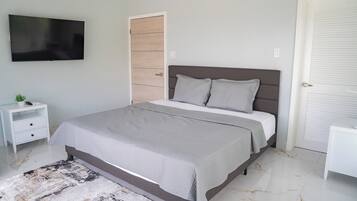 Un dormitorio moderno con una cama grande, un televisor de pantalla plana montado en la pared, una mesita de noche y una puerta con panel de madera.