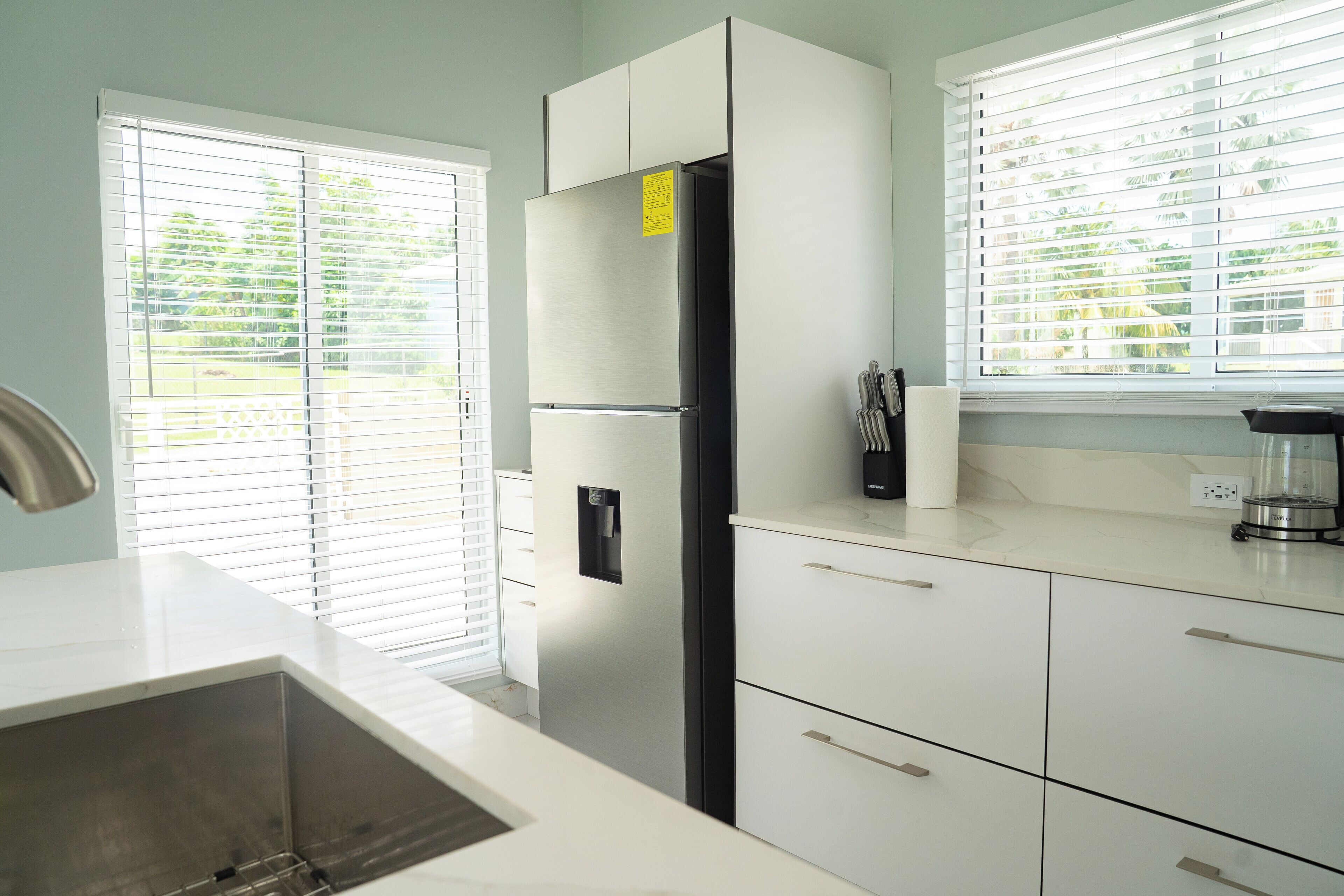 Una cocina moderna con armarios blancos, un refrigerador de acero inoxidable y una ventana con persianas.