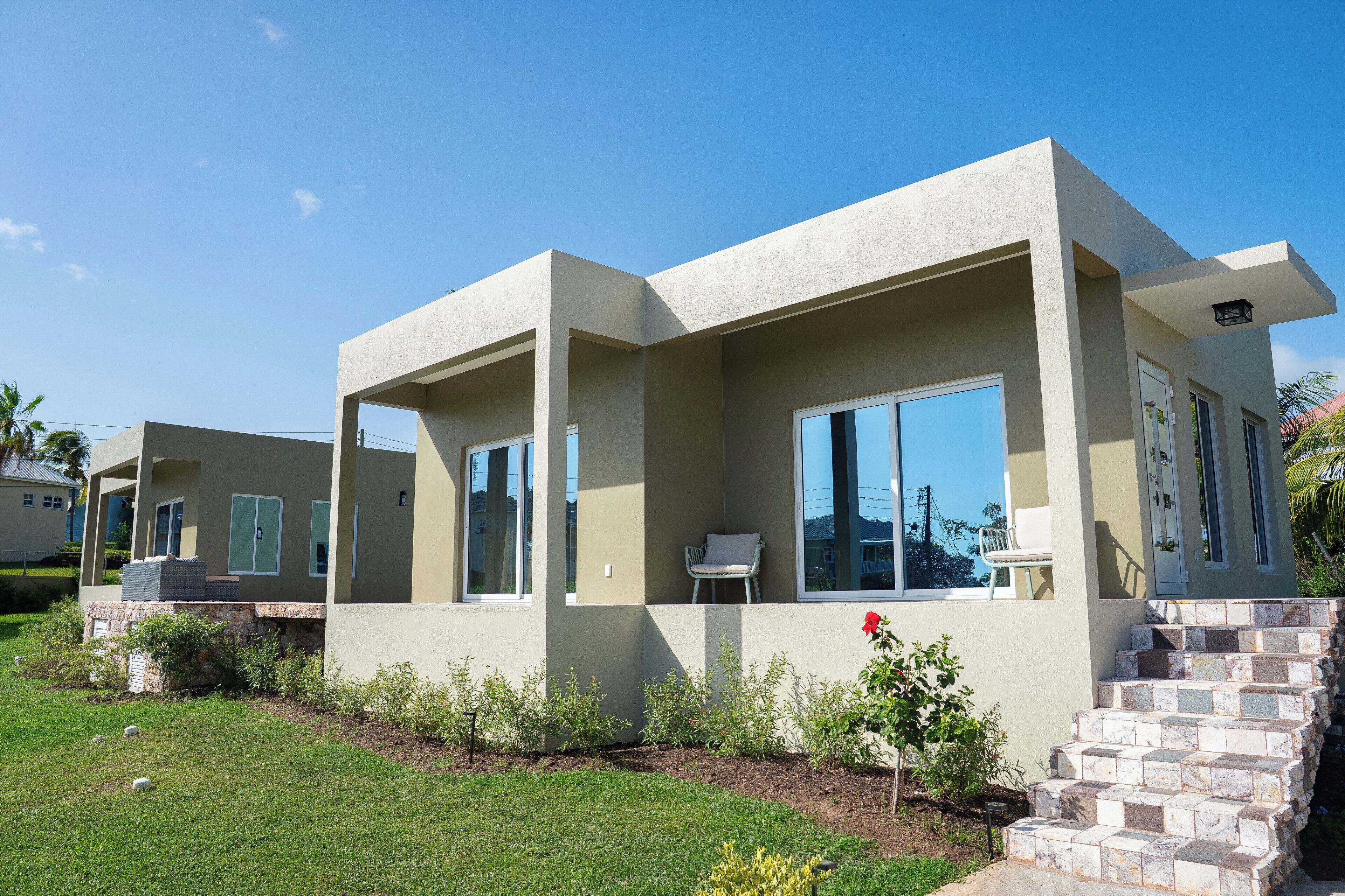 A modern two-story house with large windows, a stone staircase, and a well-maintained lawn.