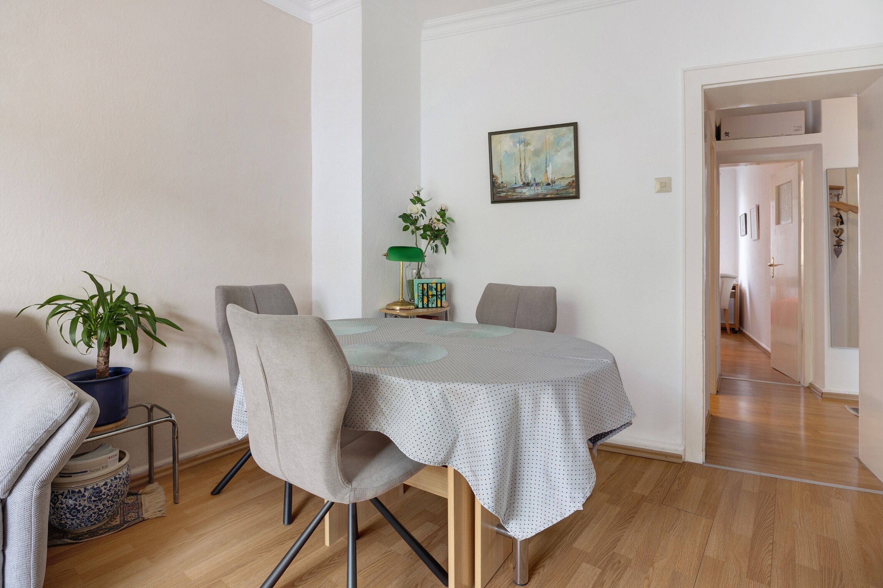 A dining area with a table, chairs, a potted plant, a lamp, and a painting on the wall.