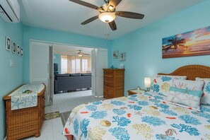 A bedroom with a bed, a dresser, a nightstand, a ceiling fan, and a painting of a sunset over the ocean. - Crucian Sunsets-Amazing sea views, resort pool, 3bd/2ba Coakley Bay Condo. (Christiansted)