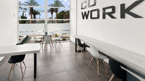 A modern office space with a large window, a 'DO WORK' sign, and a view of palm trees and buildings. - Oceana Suites Puerto Serena (La Serena)