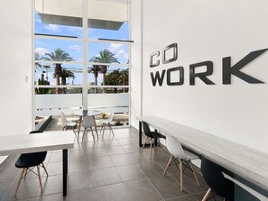 A modern office space with a large window, a 'DO WORK' sign, and a view of palm trees and buildings. - Oceana Suites Puerto Serena (La Serena)
