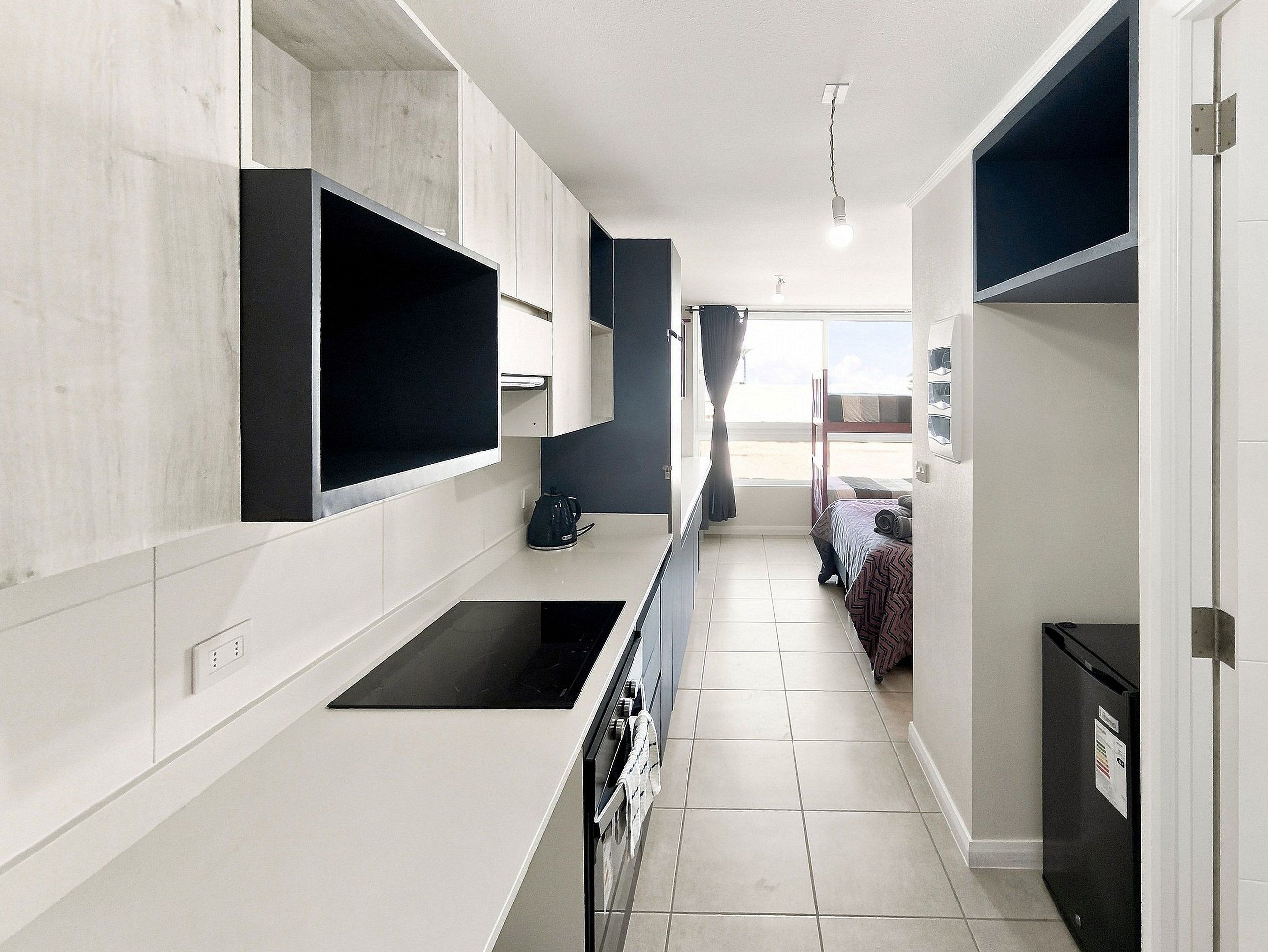 Cocina moderna y estrecha con estufa integrada, cafetera y ventana con cortinas.