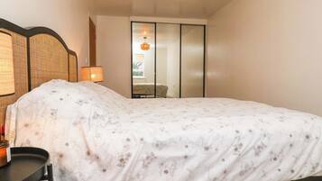 Ein Schlafzimmer mit Bett, Nachttisch, Lampe, Spiegel und einer Schiebetür zu einem weiteren Raum.