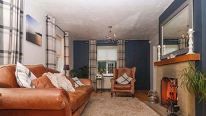 A living room with a brown leather sofa, a plaid armchair, a fluffy rug, a fireplace, and a large mirror. - Lair Close House (Harrogate)