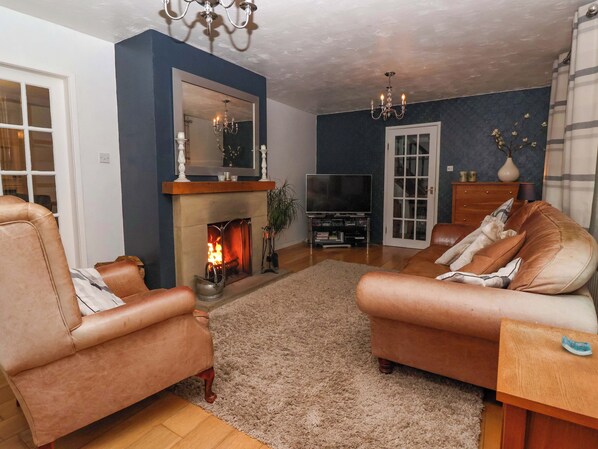 A living room with a fireplace, leather sofas, a TV, and a chandelier. - Lair Close House (Harrogate)