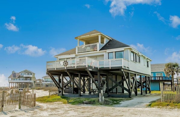 Une maison de deux étages située en bord de mer, dotée d’un balcon, construite sur pilotis et offrant une terrasse bien visible.
