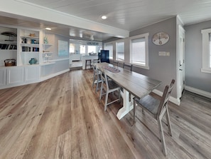 A spacious kitchen with a long wooden table, white cabinetry, and a view into the dining area.