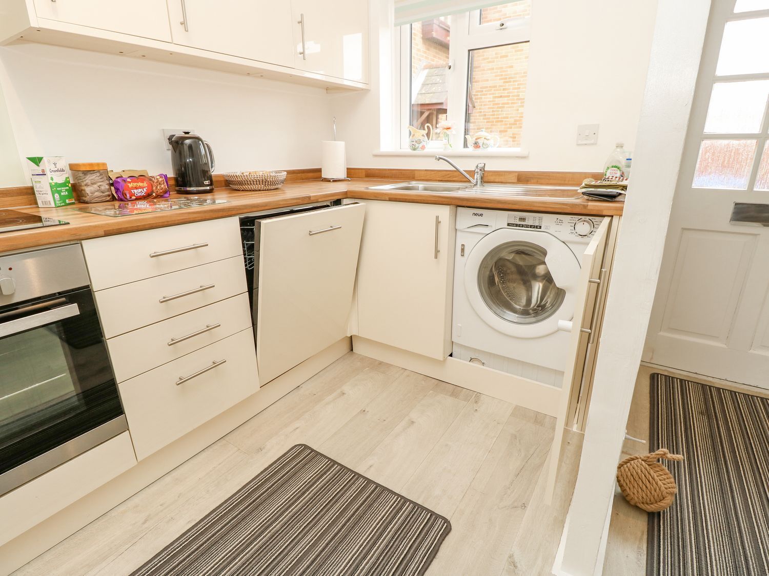 Een moderne keuken met witte kastjes, een inbouwoven, een vaatwasser en een wasmachine.