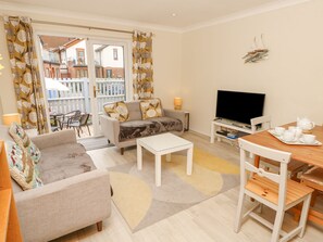 A living room with a sofa, coffee table, TV, and a dining area with a table and chairs. - Harbour View Poole (Poole)
