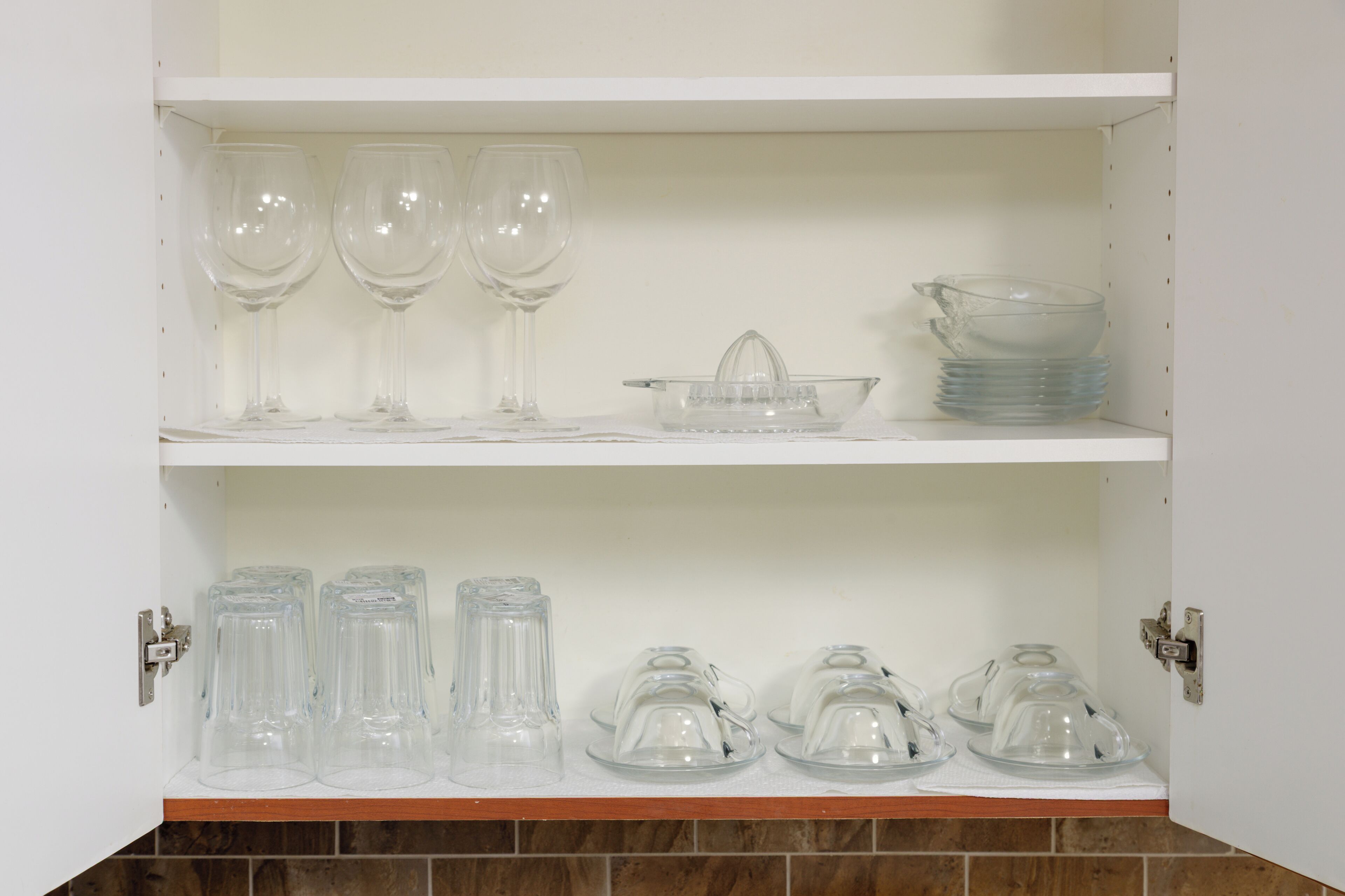 A kitchen cabinet with wine glasses, a juicer, and glass containers.