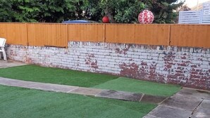 Un patio con césped artificial, un muro de ladrillo y una cerca de madera.