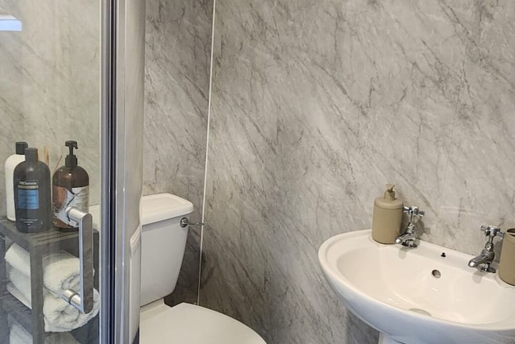 Een badkamer met een wit toilet, een glazen douchecabine, een marmeren wand en een witte wastafel met spiegel.
