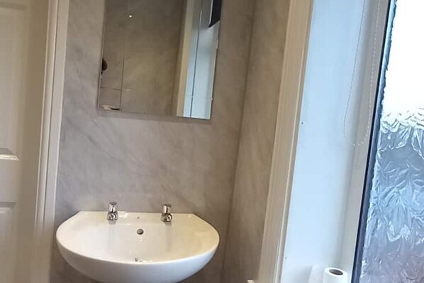 Une salle de bain avec un lavabo blanc, un miroir au-dessus et une porte en verre dépoli.
