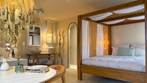 Ein Schlafzimmer mit einem hölzernen Himmelbett, einem runden Esstisch mit Stühlen und einem Schminktisch mit Spiegel und Beleuchtung.