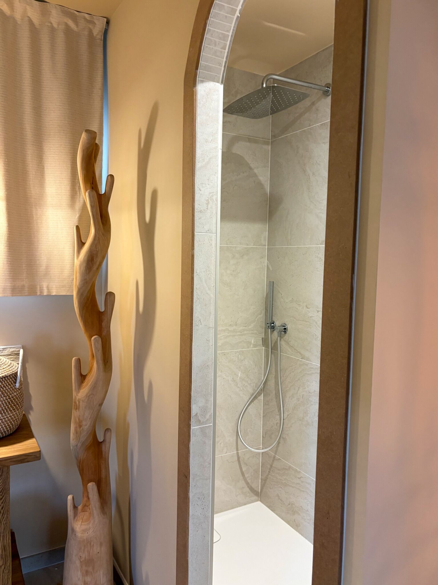 A shower with a glass door, a wooden sculpture, and a tiled wall.