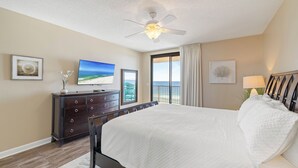 Ein Schlafzimmer mit einem großen Bett, einem Deckenventilator, einem Fernseher und einem Fenster mit Blick auf den Strand.