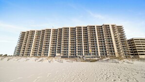 Un gran hotel con varios pisos y balcones, ubicado en una playa de arena donde se ven huellas.