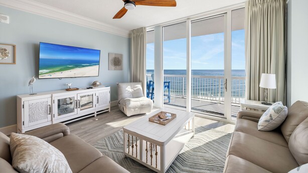 Ein geräumiges Wohnzimmer mit einem großen Fernseher, einem Deckenventilator, einem Balkon mit Meerblick und einem weißen Couchtisch.
