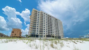 A high-rise hotel with multiple balconies, situated on a sandy beach with clear skies. - Summerchase 1007 by Liquid Life (Orange Beach)