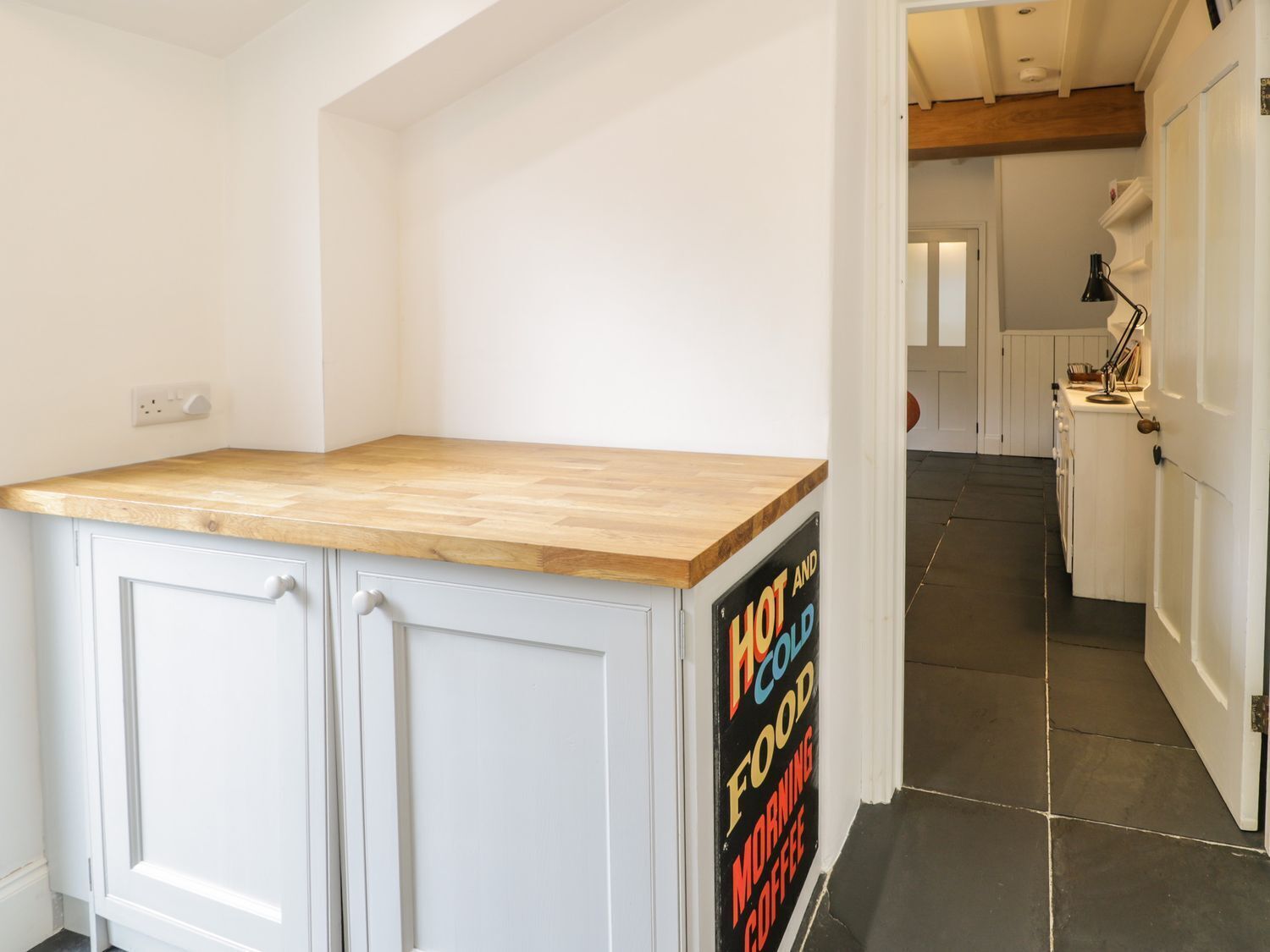 A kitchen with a wooden countertop, white cabinets, and a sign advertising hot and cold food, morning coffee.