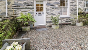 A stone building with a white door and windows, surrounded by gravel and potted plants. - Peniel Cottage (Caernarfon)