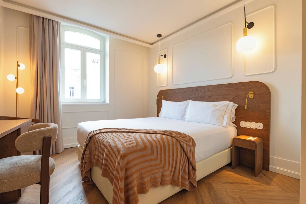 Ein ordentlich eingerichtetes Hotelzimmer mit einem Holzbett, einem Schreibtisch mit Stuhl und einem Fenster mit Vorhängen.