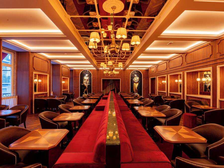 Un restaurante largo y estrecho con alfombra roja, paneles de madera y múltiples candelabros.