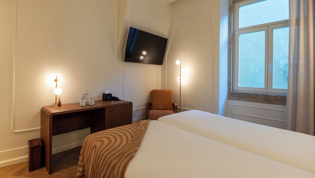 Une chambre d’hôtel équipée d’un lit, d’un bureau, d’une chaise, d’un téléviseur fixé au mur et d’une fenêtre avec des rideaux.