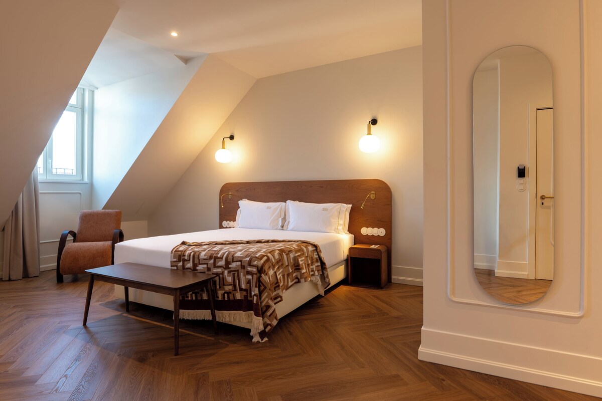 Une chambre à coucher avec un lit, des tables de chevet, une chaise, un miroir et une fenêtre.