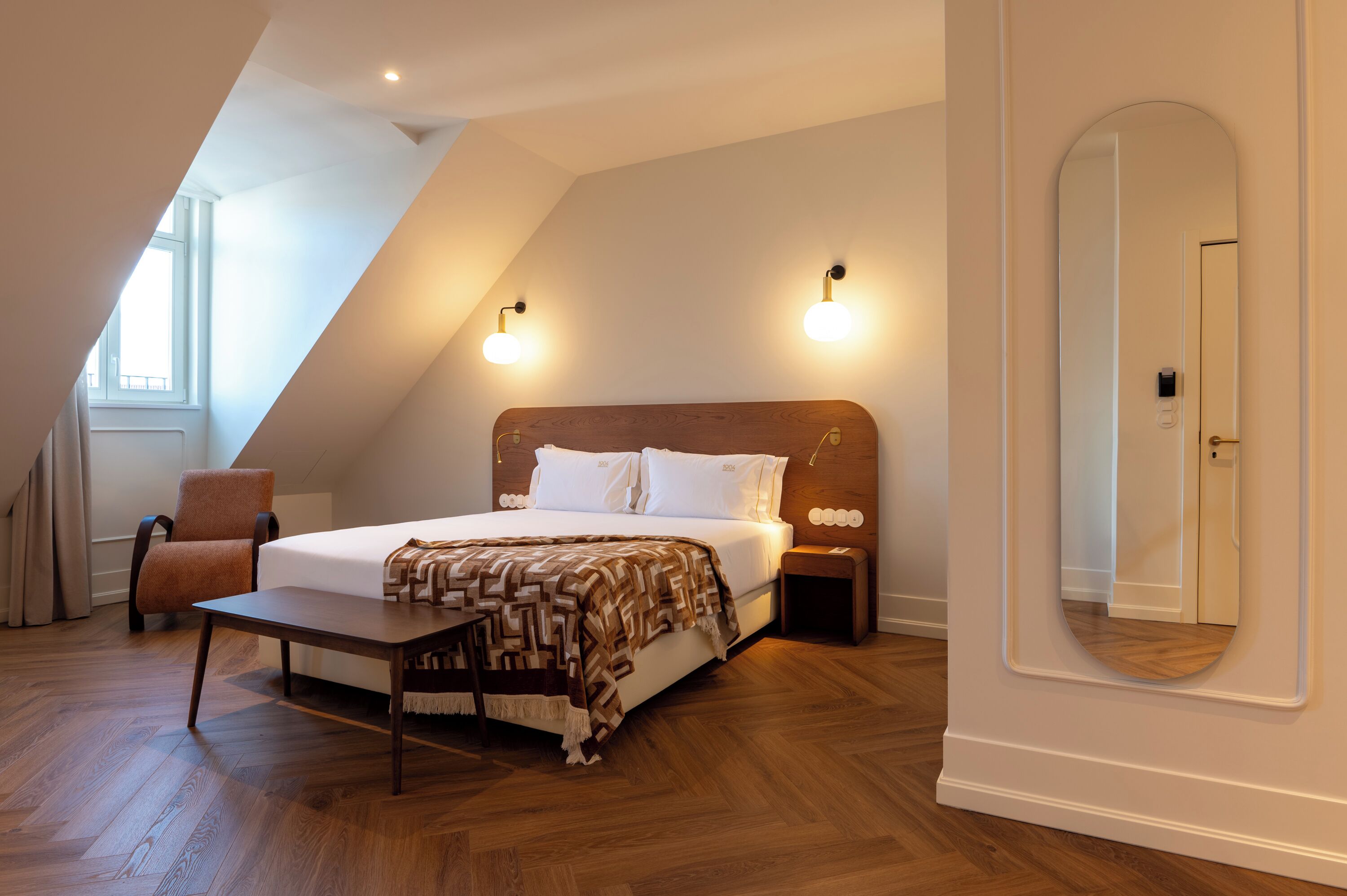 A bedroom with a bed, bedside tables, a chair, a mirror, and a window.