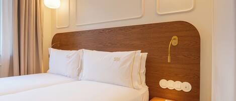 A hotel room with a wooden headboard, two white pillows, a bedside table, and wall-mounted light fixtures.