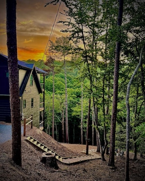 Una cabaña con terraza de madera, rodeada de árboles, y una puesta de sol al fondo.
